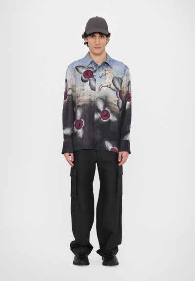 Chemise à manches longues à motifs floraux dans des tons de bleu et de noir, ornée de fleurs rouges et grises, associée à un pantalon cargo noir et une casquette grise.