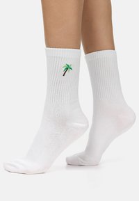 Calcetines de algodón blancos con textura acanalada, que presentan bordado de palmeras verdes y marrones en el costado. Longitud estándar de caña.
