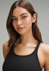 Čierny rebrovaný top na ramienka s tenkými pásikmi, ktorý má okrúhly výstrih. Hladká textúra na neutrálnom šedom pozadí.