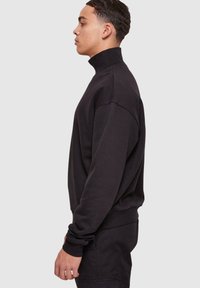 Svart høyhalset sweatshirt med ribbestrikket krage og mansjetter, med en avslappet passform og myk tekstur. Ingen synlige mønstre eller hardware-detaljer.
