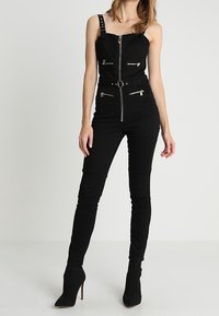 Mono negro con cremallera frontal, tirantes ajustables y múltiples bolsillos con cremallera. Presenta un diseño ajustado y una cintura ceñida con cinturón.