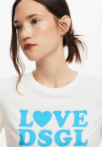T-shirt bianco con grafica blu che riporta le scritte "LOVE" e "DSGL", impreziosita da strass, collo a giro e maniche corte.