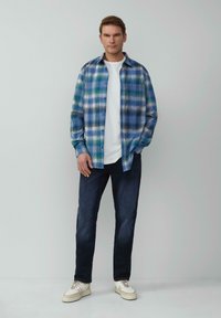 Geruite shirt in blauwe en groene tinten over een wit T-shirt, gecombineerd met donkere jeans en witte sneakers. Gladde stof, knopen vooraan.