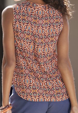 Ärmelloses Oberteil mit mehrfarbigem geometrischem Muster in Orange-, Blau- und Brauntönen, getragen mit blauer Hose.