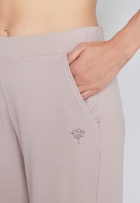 Helle rosa, weiche Stoffhosen mit einer lockeren Passform. Sie verfügen über Seitentaschen und ein kleines geprägtes Logo in der Nähe der Tasche.