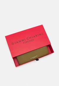 Grön texturerad plånbok i en röd låda med "GIANNI CHIARINI FIRENZE" tryckt. Har en svart dragflik och metallisk logotypdetalj.