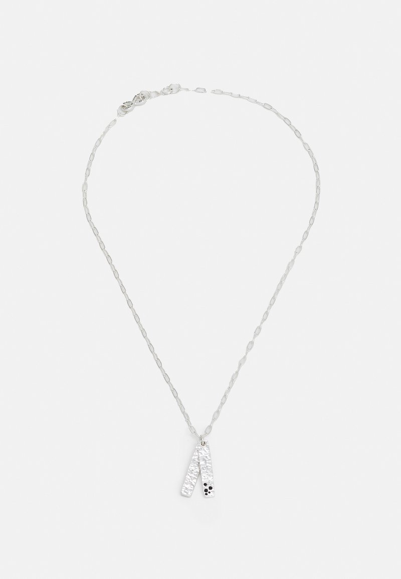 Silbernes Halsband mit einem strukturierten Anhänger, der aus zwei länglichen Stücke besteht, von denen eines kleine schwarze Punkte aufweist, und das an einer filigranen Kette hängt.