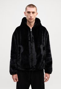 Black faux fur hoodie with a zip front, large hood, and side pockets. Features a soft texture and elastic drawstring at the hem.