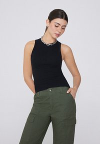 Schwarzes, geripptes Tanktop mit taillierter Passform, kombiniert mit olivgrünen Cargo-Hosen, die über mehrere Taschen und einen Knopfverschluss verfügen.