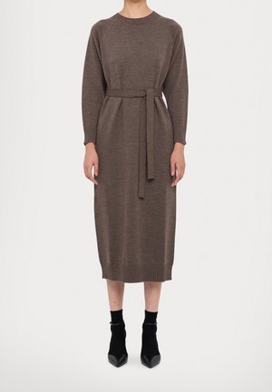 Personne portant une robe midi en maille marron à manches longues avec une ceinture à la taille, associée à des bottines noires et des chaussettes.