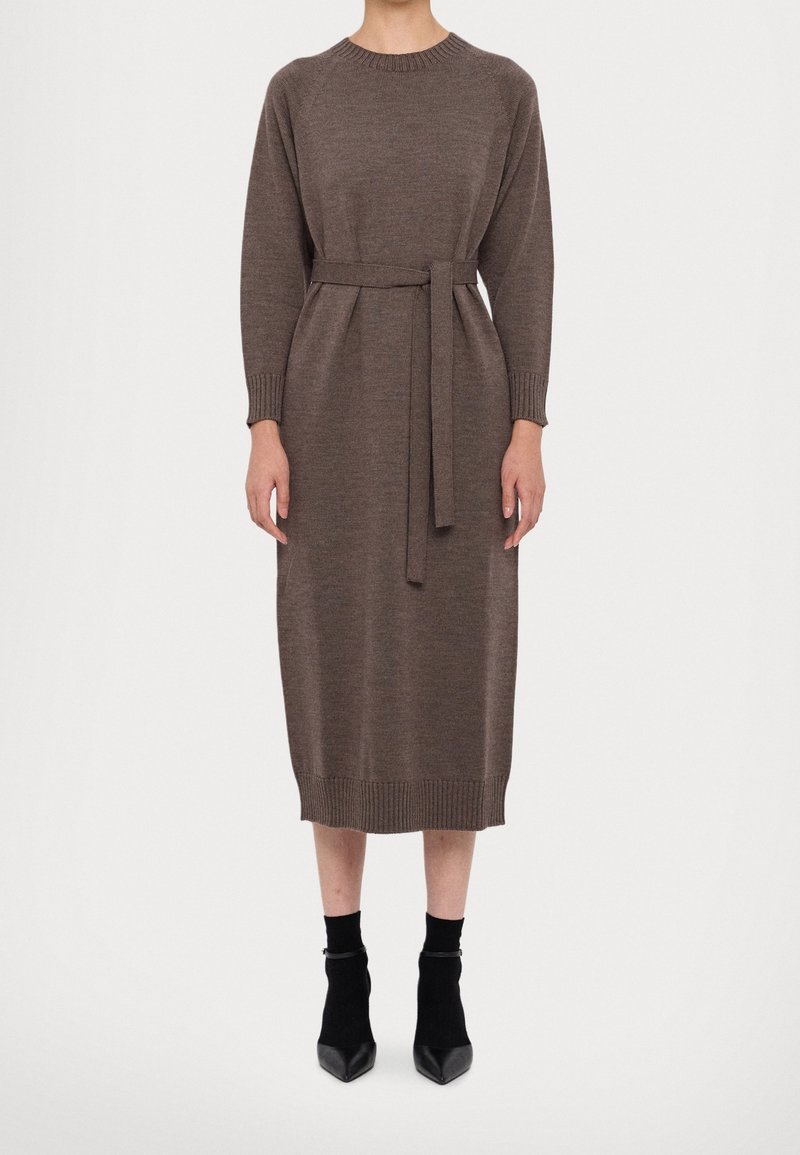 Personne portant une robe midi en maille marron à manches longues avec une ceinture à la taille, associée à des bottines noires et des chaussettes.