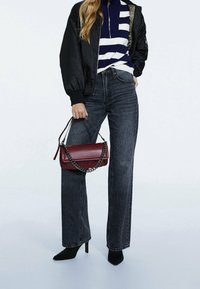 Zwarte bomberjack, marineblauwe en witte gestreepte coltrui, gewassen zwarte wijde jeans, zwarte puntige hakken, maroon handtas met kettinghengsel.