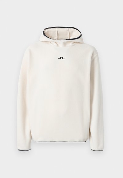 Cremfarbener Fleece-Hoodie mit hohem Kragen, schwarzen Akzenten an der Kapuze und den Ärmeln, mit einem kleinen schwarzen Logo auf der Brust.