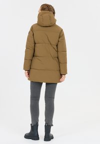 Pufferjack in khaki groen met een hoge kraag en capuchon, voorzien van een gestikt ontwerp en lange mouwen, gecombineerd met grijze skinny jeans en zwarte enkellaarsjes.