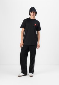 T-shirt noir à manches courtes avec une broderie de cerises rouges sur la poitrine, associé à un jean en denim noir à jambes larges et des chaussures blanches.