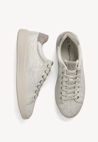 Paire de baskets basses blanches avec motif texturé, fermeture à lacets et détails beiges au talon et à la languette, vues de dessus et de côté.