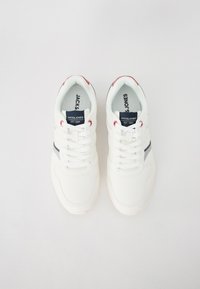 White sneakers with a textured finish, featuring blue and red accents, a lace-up design, and branded tags on the tongue.