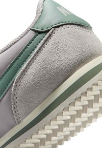 Ανδρικό αθλητικό παπούτσι από γκρι σουέτ και ύφασμα με πράσινες λεπτομέρειες, υφή με ανάγλυφο μοτίβο, λαστιχένια σόλα με σχεδιασμένο πέλμα και ραμμένες λεπτομέρειες.