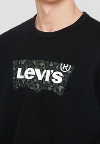 Felpa nera con logo Levi's a stampa leopardata verde sul petto, con collo a giro e tessuto testurizzato.