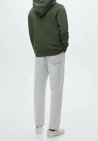 Felpa verde oliva con cappuccio, abbinata a pantaloni dritti grigi chiari e sneakers bianche. L'outfit presenta un design semplice e linee pulite.
