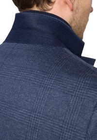 Granatowa marynarka w kratę o teksturowanej powierzchni i ciemnym kołnierzu. Posiada usztywnione szwy oraz nowoczesny krój z tyłu.