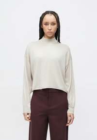 Jasnobeżowa bluzka z długim rękawem, z wysokim kołnierzem, luźnym fasonem i prążkowanymi mankietami, zestawiona z wysokimi, ciemnoczerwonymi spodniami w burgundowym kolorze.