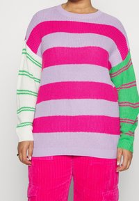 Överdimensionerad stickad tröja med lila, rosa och vita ränder; grönrandig detalj på en ärm; texturerat stickat mönster.