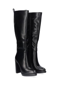Botas de cuero negras hasta la rodilla con una textura suave, tacón alto y cuadrado, punta redonda y cremallera lateral. Con una cinta en la parte posterior.