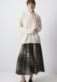 Maglione beige lavorato a maglia con colletto alto e polsini a coste, abbinato a una lunga gonna fluida con stampa leopardata nera e marrone.