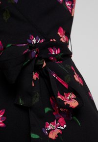 Robe en tissu noir avec des motifs floraux vifs en rose et violet. Comprend un détail de taille nouée pour un look ajusté. Texture lisse.