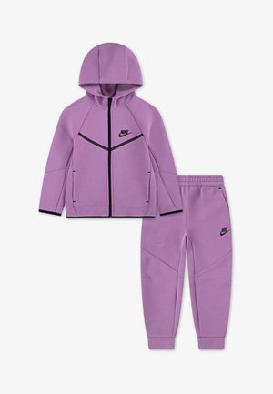 Fialová mikina na zips s kapucňou a čiernymi detailmi, v kombinácii s rovnakými fialovými teplákmi so šikmými švami a vreckami.