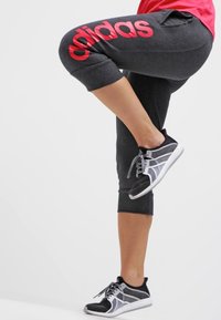 Zwarte sportieve capribroek met groot rood "adidas" logo, voorzien van zakken en gestructureerde zoom, gecombineerd met zwart-witte sneakers.