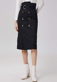 Jupe crayon noire taille haute avec un détail de boutons dorés à double boutonnage et une taille ceinturée. Présente une fente sur le côté et une texture de tissu lisse.