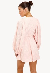 Roze jurk met pofmouwen, bloemenborduurwerk, elastische taille en een uitlopende rok. Getextureerde stof voegt diepte en detail toe.