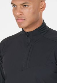 Svart halvdraget pullover med en låg krage, med en texturerad bröstficka och slätt tyg, designad för komfort och funktionalitet.