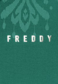 Un tessuto verde con una texture a coste presenta la parola "FREDDY" in lettere metalliche argentate, accompagnata da un intricato motivo sbiadito.