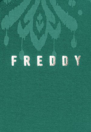 Un tessuto verde con una texture a coste presenta la parola "FREDDY" in lettere metalliche argentate, accompagnata da un intricato motivo sbiadito.