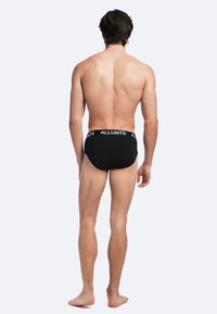 Black briefs with a branded waistband, featuring a smooth texture and snug fit. View shows the back and legs of the model.