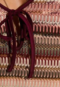 Top de encaje con patrones de zigzag multicolores en tonos burdeos, rosa y crema; acabado con un lazo burdeos en el cuello.