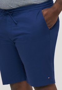 Marineblå shorts lavet af letvægtsstof med snoretræk i taljen, sidelommer og en lille logoaccents ved sømmen.