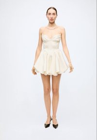 Strapless cream mini dress with a fitted bodice, flared skirt, and draped detailing. Worn with black pointed-toe heels.