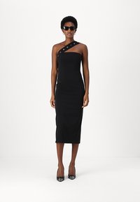 Crna, tijelu priljubljena midi haljina s jednim ramenskim trakama koja sadrži metalne okove. Glatka tkanina i elegantan kroj, uparen s crnim potpeticama.