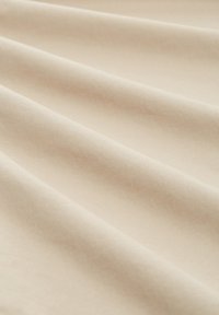 Bežani pamučni materijal s glatkom teksturom, s mekim naborima i dosljednim završetkom, stvarajući ravni, drapirani izgled.