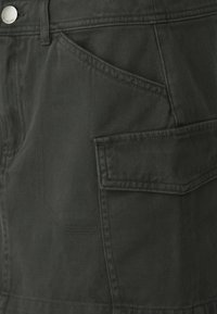 Pantaloni cargo in tessuto verde scuro con finitura testurizzata. Presentano numerose tasche e cuciture a contrasto per una maggiore resistenza.