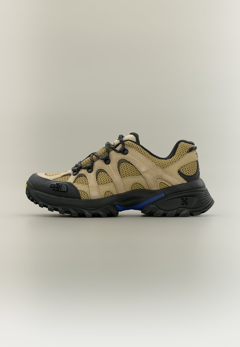 Μπεζ και μαύρο παπούτσι πεζοπορίας με πλέγμα πάνελ, μαύρα κορδόνια, ανθεκτική σόλα και το λογότυπο The North Face στο καπάκι του δακτύλου.