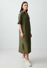 Olijfgroene linnen jurk, knielang met een kraag, korte mouwen, zijsplit, textuurstof, gecombineerd met witte sneakers.