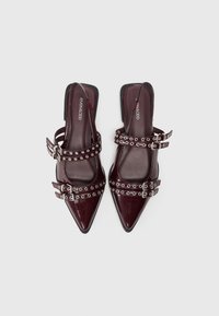 Talons slingback en vernis bourgogne avec bouts pointus, dotés de deux sangles ajustables avec œillets en argent et boucles. Doublure intérieure lisse.