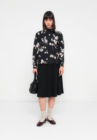 Top nero a maniche lunghe con fiori, dettagli rosa, abbinato a una gonna nera. Gli accessori includono una borsa nera piccola e delle scarpe flat bordeaux. Calzini neutri.