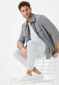 Gray button-up shirt over a white t-shirt, paired with light gray joggers and white sneakers. Smooth fabrics and casual fit.