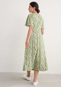 Vihreä kukallinen midi-mekko lyhythihaisena, jossa on lehtikuvio ja rento malli, yhdistettynä valkoisiin tennareihin.